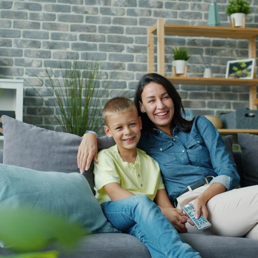 A mother and her young son laughing together on the sofa after school
